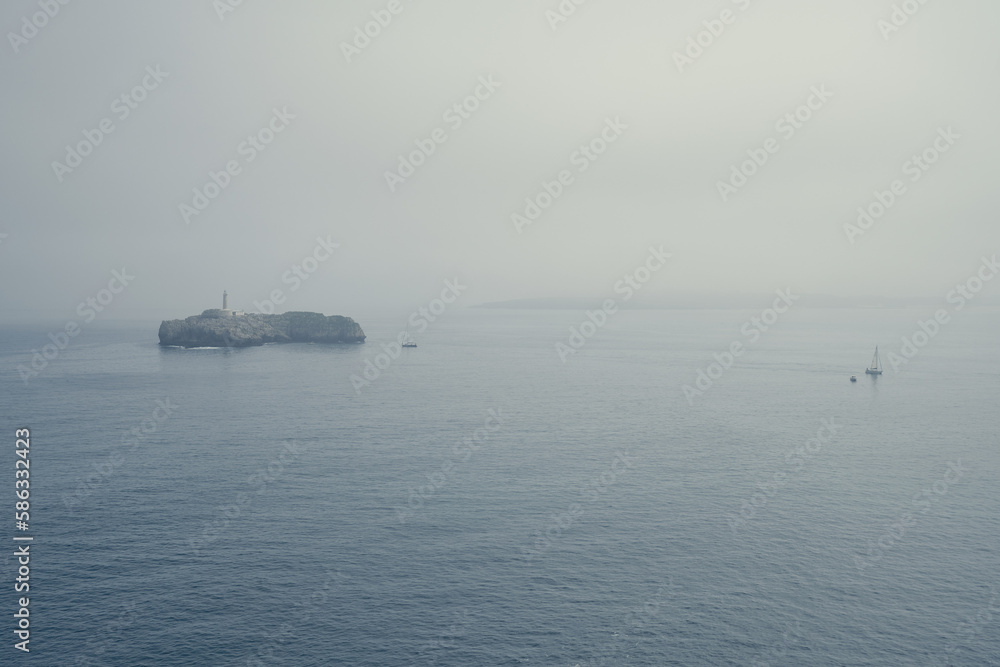 A view of a sea landscape with a small island in it during a foggy morning