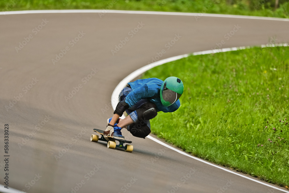 Obraz premium A guy wearing a helmet is riding his longboard on a country road