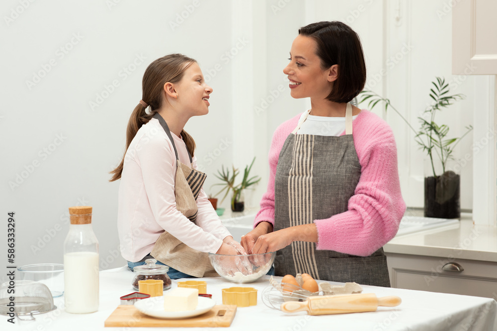 Cheerful caucasian young mother and teen daughter in aprons make dough with hands for cookie, talk, have fun Cheerful caucasian young mother and teen daughter in aprons make dough with hands for cookie, talk, have fun