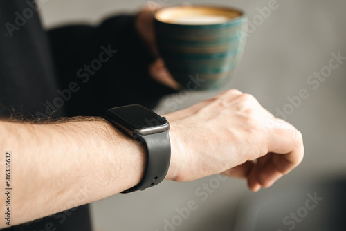 Man with cup of coffee checking time on her smart watch during working, business and technology concept, close up, copy space.