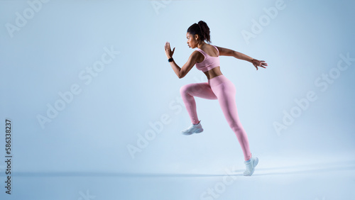 Sporty african american lady running in mid air over blue neon background, panorama with free space