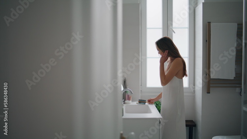 Young woman brushing hair in bathroom. Tender girl applying mask after shower