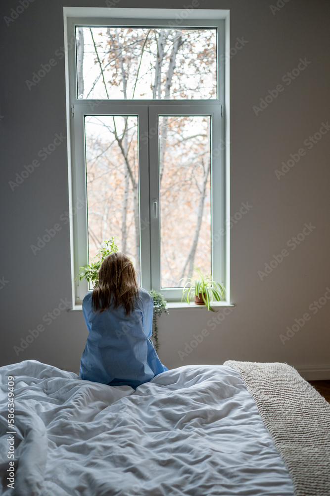 Rear view of lonely woman sitting on bed at home, sad single female feeling depressed, thinking of life purpose, coping with loneliness after break up. Women and depression concept Rear view of lonely woman sitting on bed at home, sad single female feeling depressed, thinking of life purpose, coping with loneliness after break up. Women and depression concept