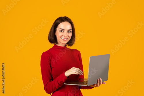 Happy young woman digital nomad using laptop on orange