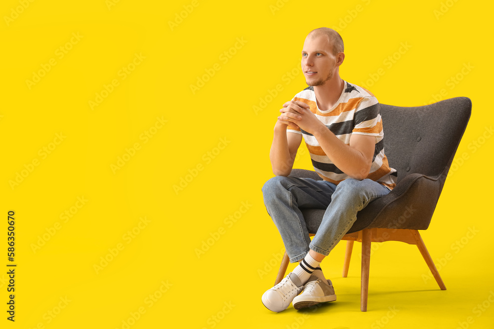 Handsome man sitting in black armchair on yellow background