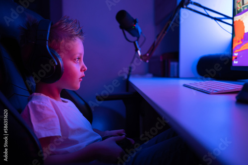 A little boy with headphones and a microphone plays computer games. Streams console games 