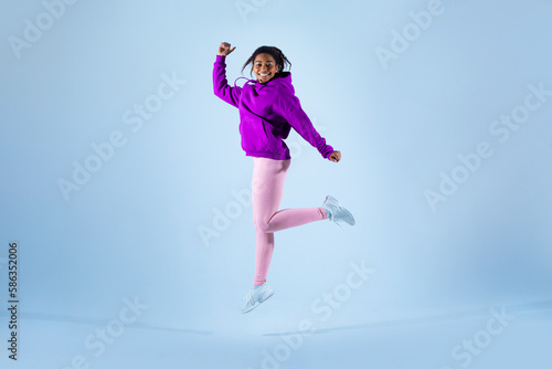 Cheerful black woman in sportswear having fun jumping high on blue background  studio shot  full length