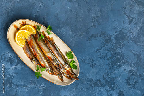 Plate with delicious smoked capelin on blue grunge background photo