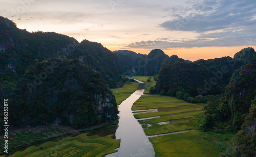 Aerial top view of fresh paddy rice and lake river  green agricultural fields with mountain hills valley in countryside or rural area of Ninh Binh  in Asia  Vietnam. Nature landscape background.