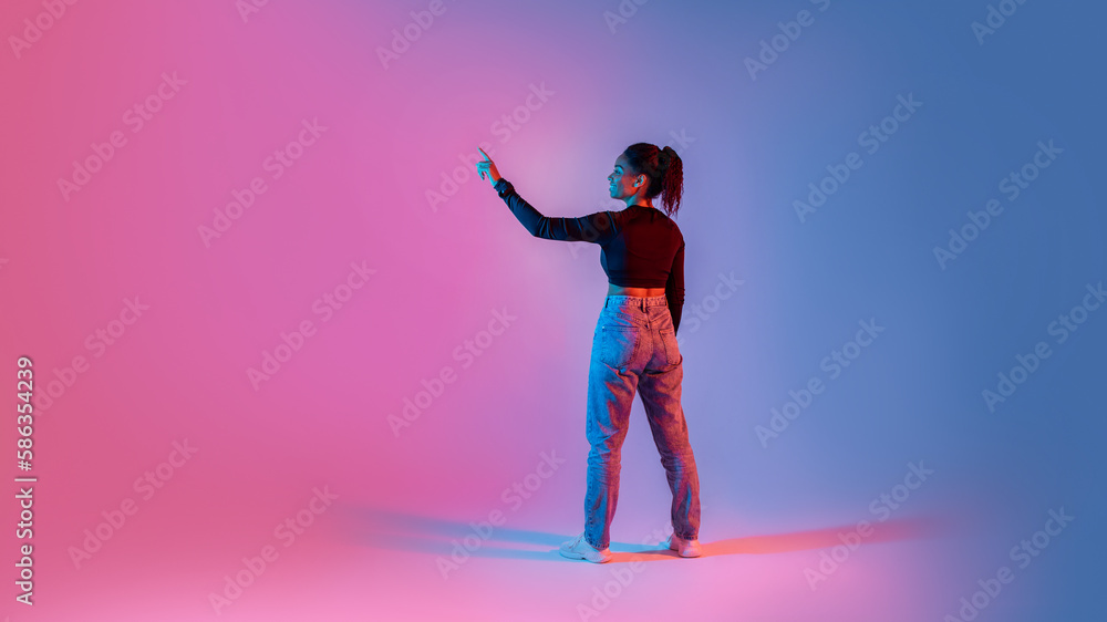 Back view of black lady touching imaginary screen, using virtual interface on colorful neon background, panorama Back view of black lady touching imaginary screen, using virtual interface on colorful neon background, panorama