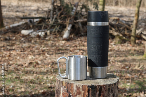 A thermos and a tin mug with tea  snack on a trip in  the forest