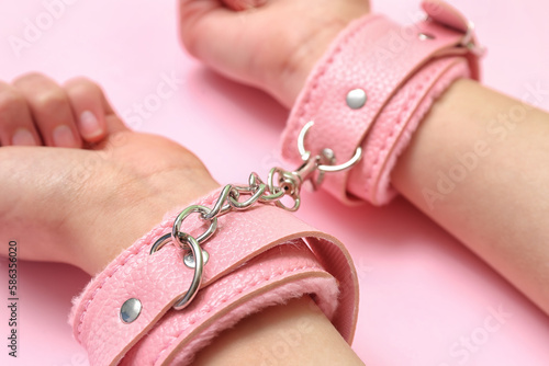 Woman with handcuffs from sex shop on pink background, closeup photo