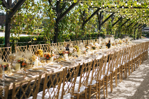Wedding decorations. Served wedding table with golden plates, golden chairs, napkins, decorative fresh and dried flowers, candles and light bulbs. Celebration details, wedding outdoor 