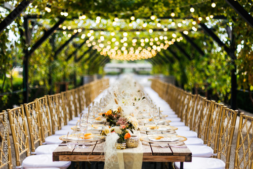 Wedding decorations. Served wedding table with golden plates, golden chairs, napkins, decorative fresh and dried flowers, candles and light bulbs. Celebration details, wedding outdoor	
