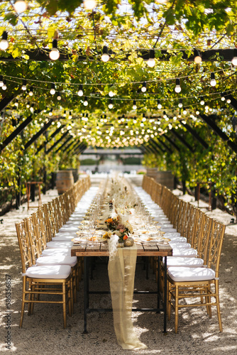 Wedding decorations. Served wedding table with golden plates, golden chairs, napkins, decorative fresh and dried flowers, candles and light bulbs. Celebration details, wedding outdoor	
