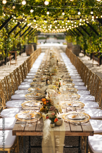 Wedding decorations. Served wedding table with golden plates, golden chairs, napkins, decorative fresh and dried flowers, candles and light bulbs. Celebration details, wedding outdoor	
