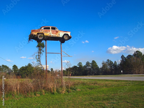 Old Rusting Car On Top Of Poles Roadside