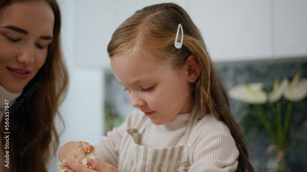 Young mother teaching daughter cooking indoor portrait. Focused kid making dough Young mother teaching daughter cooking indoor portrait. Focused kid making dough