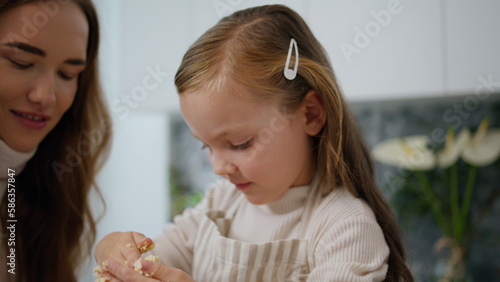 Young mother teaching daughter cooking indoor portrait. Focused kid making dough