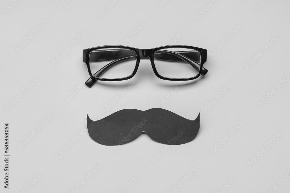 Eyeglasses and black paper mustache on grey background Eyeglasses and black paper mustache on grey background