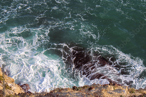 Dark turquoise waves breaking on black rocks, rolling tide, bird's eye view. Ocean photography. 