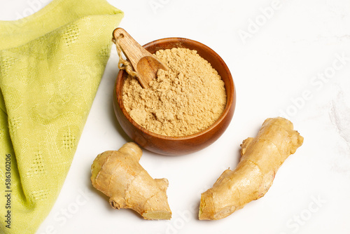 Jengibre en polvo dentro de un cuenco de madera de bambú junto a una raíz  y una servilleta verde sobre un fondo de mármol texturado. Vista superior y de cerca. Copy space