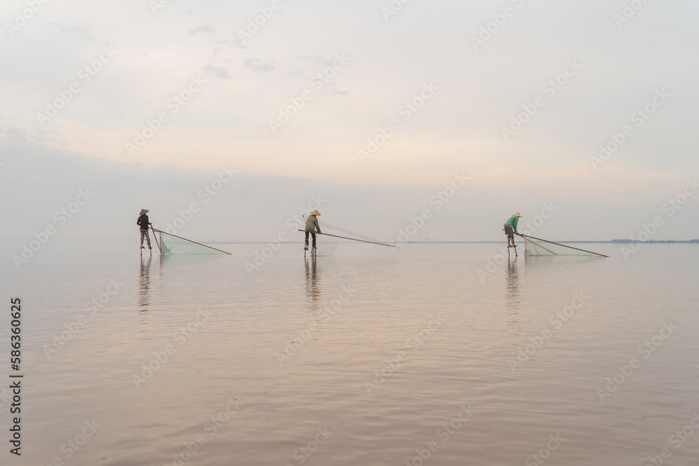 Silhouette of Vietnamese fisherman holding a net for catching freshwater fish in nature lake or river with reflection in morning time in Asia in Vietnam. People.