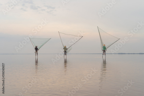 Silhouette of Vietnamese fisherman holding a net for catching freshwater fish in nature lake or river with reflection in morning time in Asia in Vietnam. People.