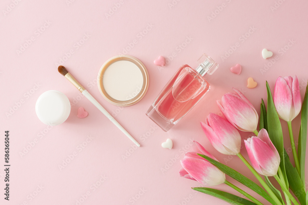 Top view composition of bunch of pink tulips perfume bottle cosmetic brush makeup powder cream jar and colorful hearts on isolated pastel pink background. Mother's Day atmosphere concept. Top view composition of bunch of pink tulips perfume bottle cosmetic brush makeup powder cream jar and colorful hearts on isolated pastel pink background. Mother's Day atmosphere concept.