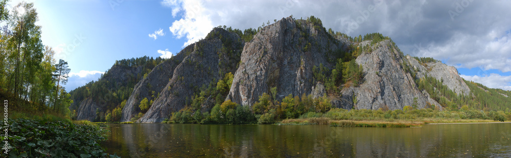 An amazing panorama of a majestic limestone rock illuminated by evening light on a fast river on a beautiful autumn day.