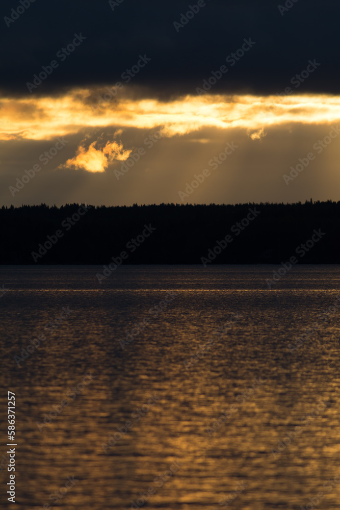 Light shining through dark clouds over a forest and a lake Light shining through dark clouds over a forest and a lake