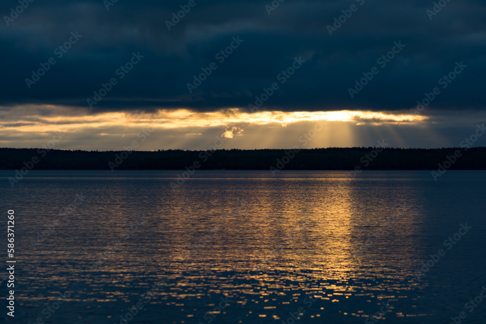 Light shining through dark clouds over a forest and a lake