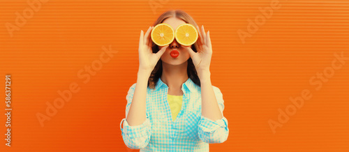 Summer portrait of happy cheerful smiling woman covering her eyes with slices of orange and looking for something on background