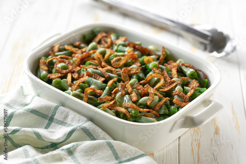 green bean casserole with crispy fried shallots onions on a white wooden table.