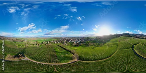 360 panorama aerial drone view above the Uffholtz and Wattwiller villages green vineyard hills in a Alsatian valley by sunny day with blue sky, dark stormy clouds in the distance, with paths