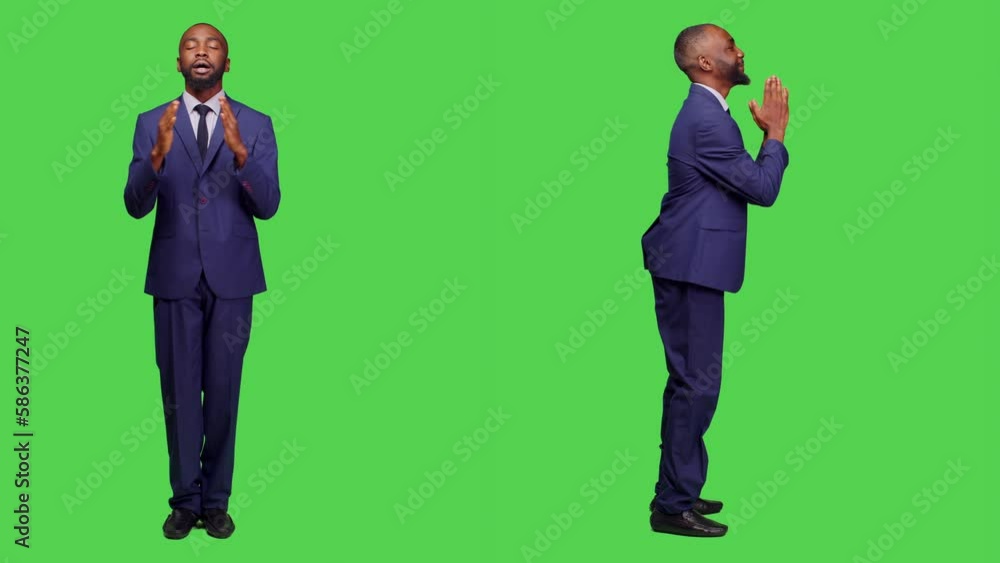 Startup entrepreneur praying to god for good luck in studio, wearing formal suit over green screen backdrop. Young male employee holding hands in a prayer sign, religious person. Startup entrepreneur praying to god for good luck in studio, wearing formal suit over green screen backdrop. Young male employee holding hands in a prayer sign, religious person.