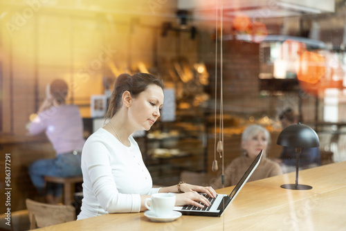 Young woman spending time in cozy coffeehouse with laptop and coffee