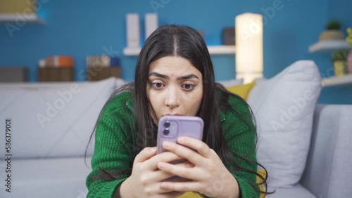 Shocked young woman looking at phone.
The young woman looking at the phone at home is bewildered and cannot believe it.
