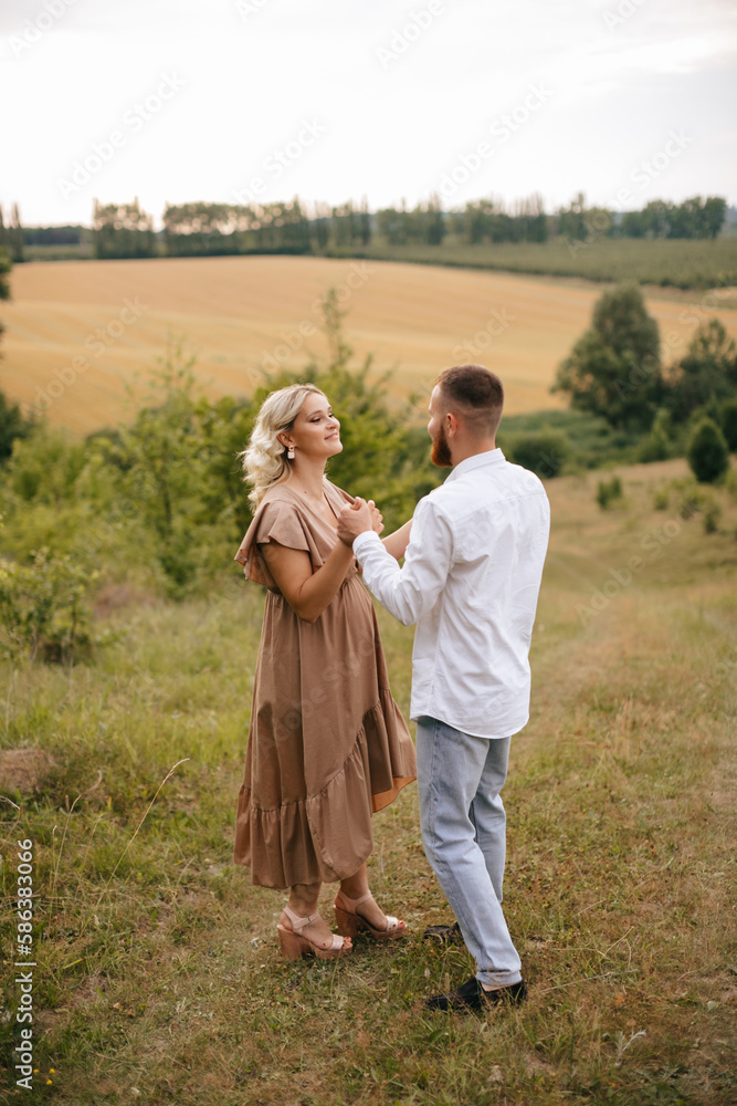 A man is holding hands his pregnant wife in a field at sunset. A man is holding hands his pregnant wife in a field at sunset.