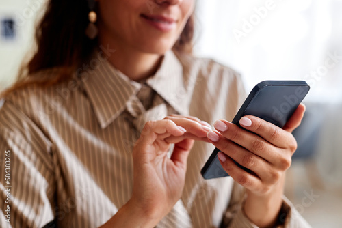 Close up of smiling young woman holding smartphone and tapping screen, copy space
