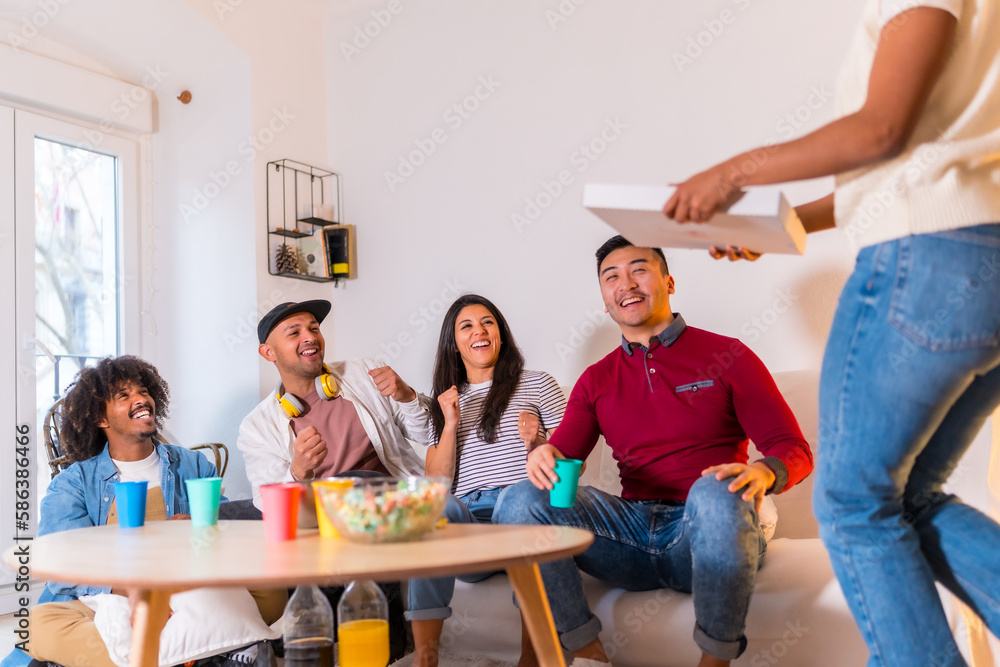 Group of multi-ethnic friends on a sofa eating pizza and drinking soft drinks at a home party, very happy receiving the girl with the pizza Group of multi-ethnic friends on a sofa eating pizza and drinking soft drinks at a home party, very happy receiving the girl with the pizza