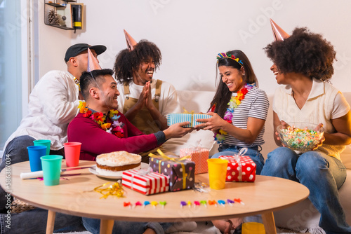 Group of friends at a birthday party on the sofa at home smiling delivering the gifts  surprising the birthday girl