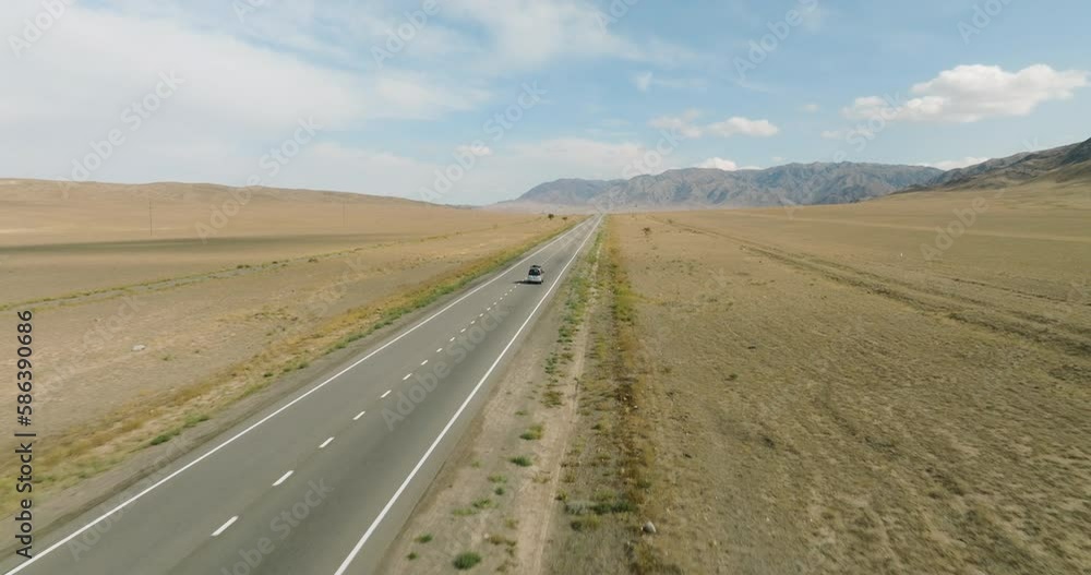 One gray silver wagon car driving alone, travel on empty straight asphalt road freeway through empty arid steppe plain at summer sunny day. Aerial drone wide into the distance view. One gray silver wagon car driving alone, travel on empty straight asphalt road freeway through empty arid steppe plain at summer sunny day. Aerial drone wide into the distance view.