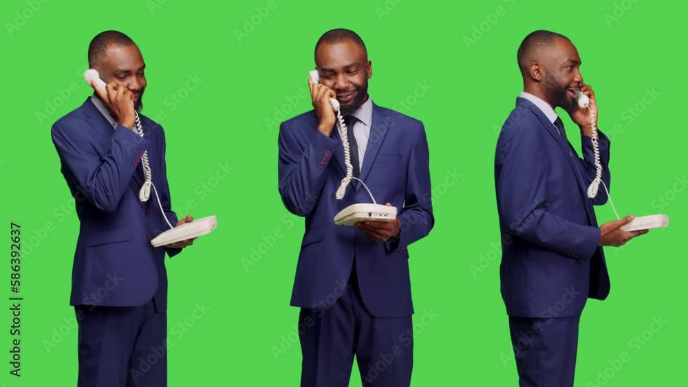 African american man using landline phone to call manager, answering office telephone with cord for remote chat in studio. Male employee posing on green screen background, business suit. African american man using landline phone to call manager, answering office telephone with cord for remote chat in studio. Male employee posing on green screen background, business suit.