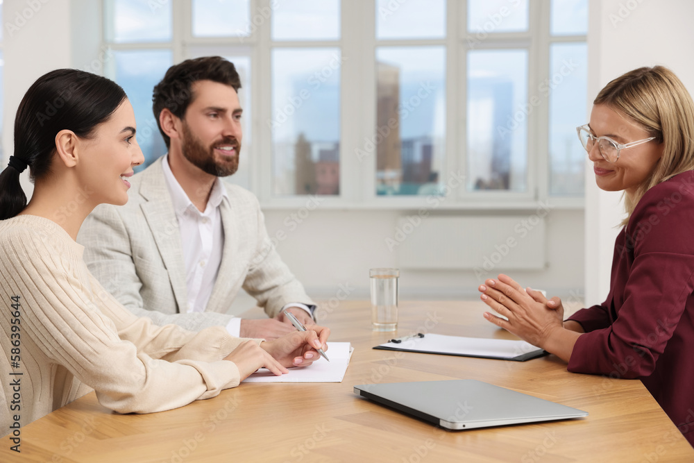 Real estate agent and couple signing contract at table in new apartment Real estate agent and couple signing contract at table in new apartment