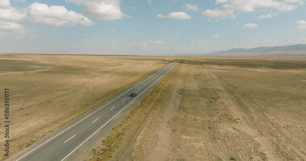 One black sedan car driving alone, travel on empty straight asphalt road freeway through empty arid steppe plain at summer sunny day. Aerial drone wide into the distance view. One black sedan car driving alone, travel on empty straight asphalt road freeway through empty arid steppe plain at summer sunny day. Aerial drone wide into the distance view.