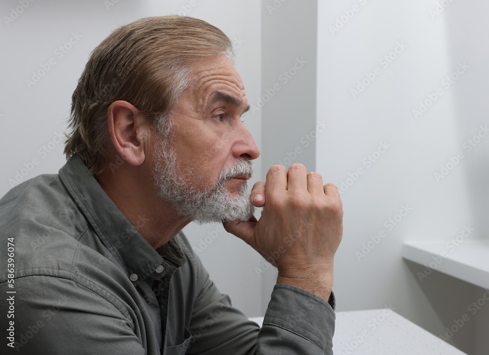 Upset senior man looking at window indoors, space for text. Loneliness concept Upset senior man looking at window indoors, space for text. Loneliness concept