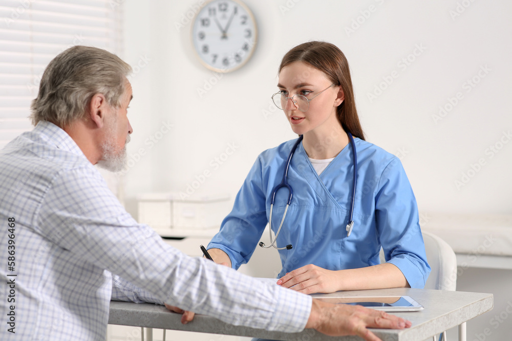 Doctor filling patient's medical card at table in clinic Doctor filling patient's medical card at table in clinic