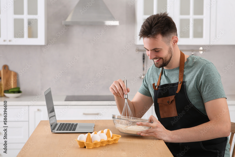 Happy man learning to cook with online video on laptop at table in kitchen. Time for hobby Happy man learning to cook with online video on laptop at table in kitchen. Time for hobby