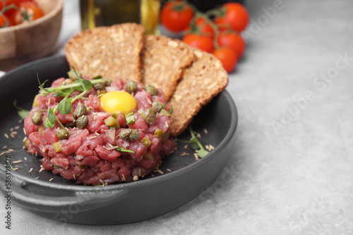 Tasty beef steak tartare served with yolk, capers and bread on light grey table. Space for text